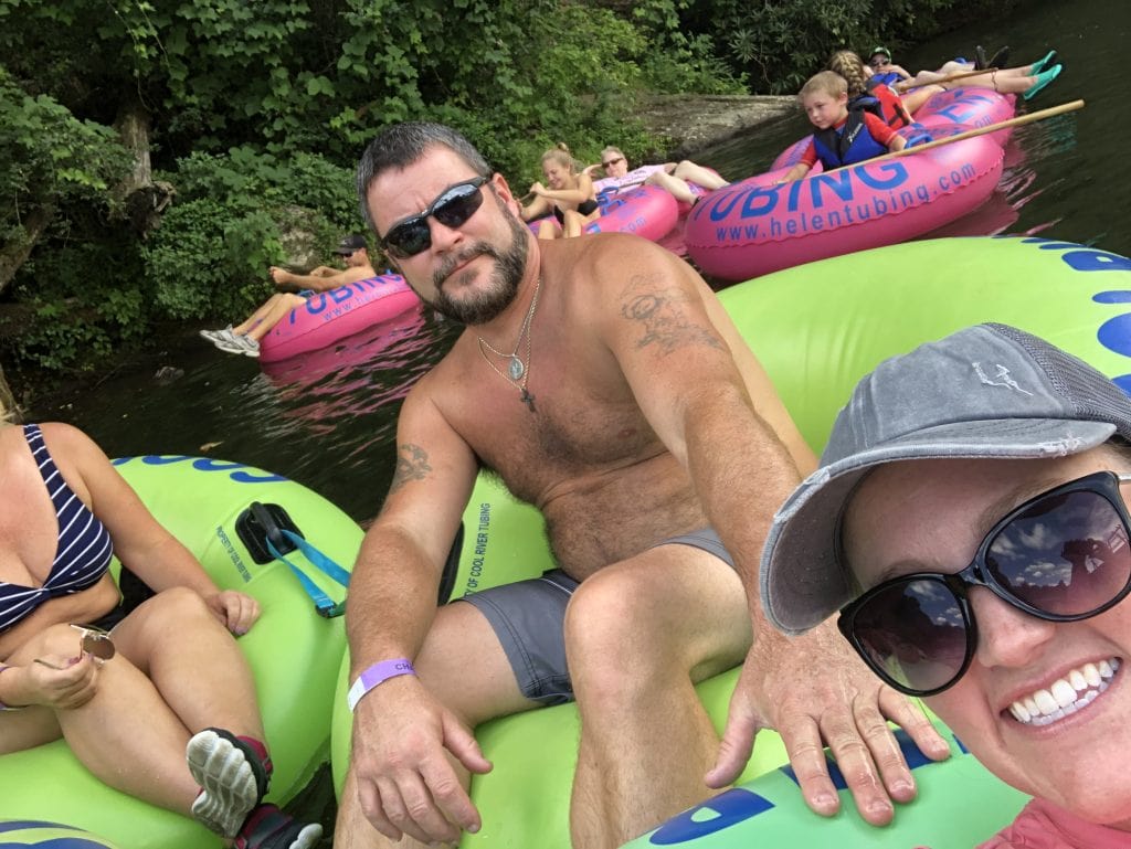 A group of people enjoy a sunny day tubing down the Chattahoochee River in Helen, Georgia, floating in bright green and pink inner tubes from Helen Tubing. Surrounded by lush greenery, the relaxed scene captures a popular summer activity in North Georgia.