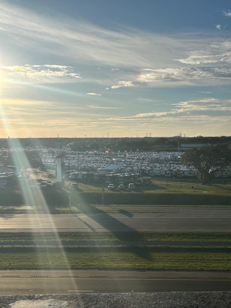 Aerial view of the Tampa RV Show at sunset, with rows of RVs densely packed into a lot beside a highway. Long shadows and soft golden light stretch across the scene, highlighting the scale of this major RV event.