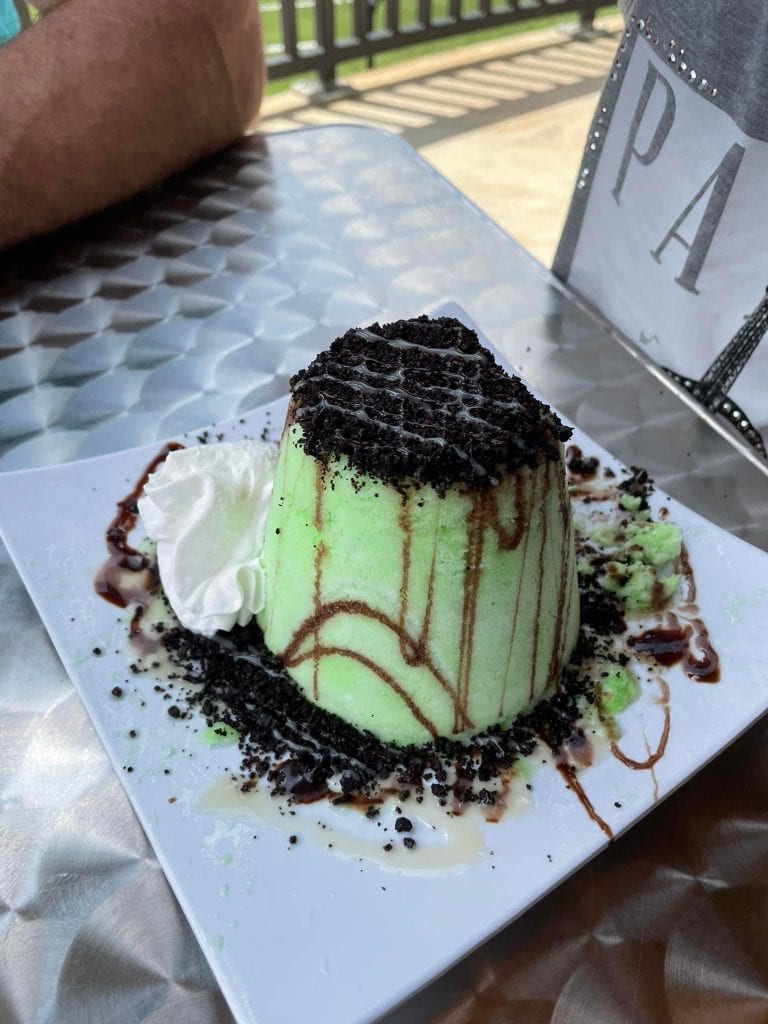 Mint green shaved snow dessert from Vampire Penguin, topped with crushed Oreos and drizzled with chocolate and condensed milk. Served with a dollop of whipped cream on a white plate with cookie crumbles around the base.