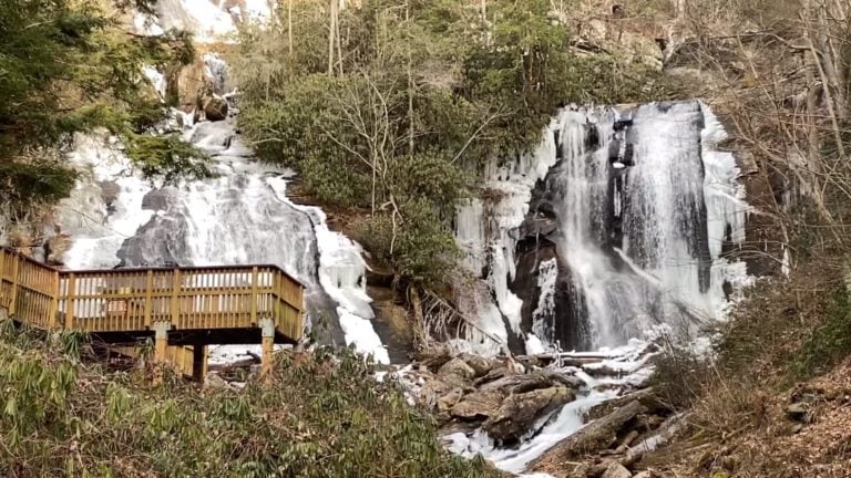 Frozen cascades at Anna Ruby Falls in North Georgia, with ice clinging to the rocks and trees around the double waterfall. A wooden viewing platform stands in the foreground, making this a scenic and accessible stop for winter hikes and things to do in North Georgia.
