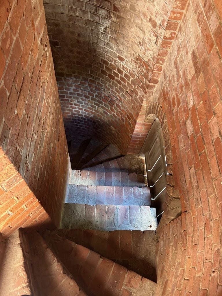 Brick spiral staircase inside Fort Clinch, with warm light highlighting the curved masonry walls and worn stone steps. The narrow passageway showcases the fort’s historic 19th-century architecture and craftsmanship.