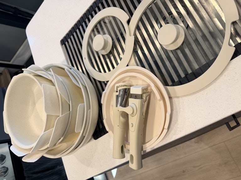 Overhead view of the cream-colored Gourmetific™ Cookware Set neatly arranged on a kitchen counter, including stackable nonstick pots and pans with protective inserts, three glass lids, and two detachable handles. The sleek, space-saving design highlights the set’s compact storage appeal.