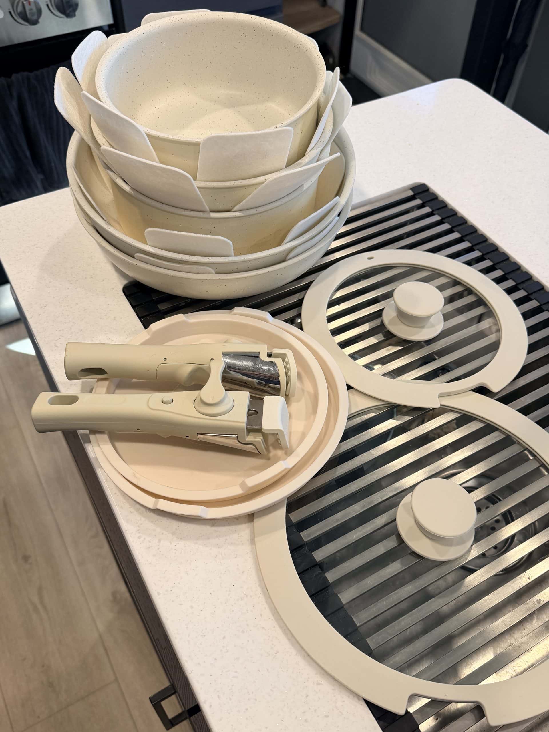 Overhead view of the cream-colored Gourmetific™ Cookware Set neatly arranged on a kitchen counter, including stackable nonstick pots and pans with protective inserts, three glass lids, and two detachable handles. The sleek, space-saving design highlights the set’s compact storage appeal.