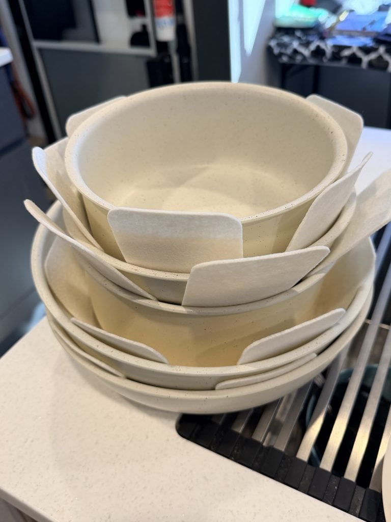 A close-up of the cream-colored Gourmetific™ cookware stack, neatly nested with felt protectors between each pot and pan. The image showcases the set’s space-saving, nonstick design and careful storage setup.