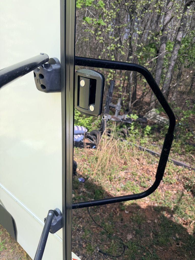 Standard black RV door lock with a pull handle mounted on the edge of a beige camper door before upgrading to a keypad entry system.